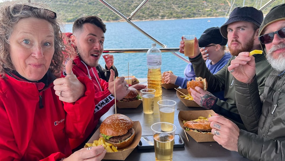 Group enjoying lunch on a cruise near Split, with burgers, fries, and drinks.