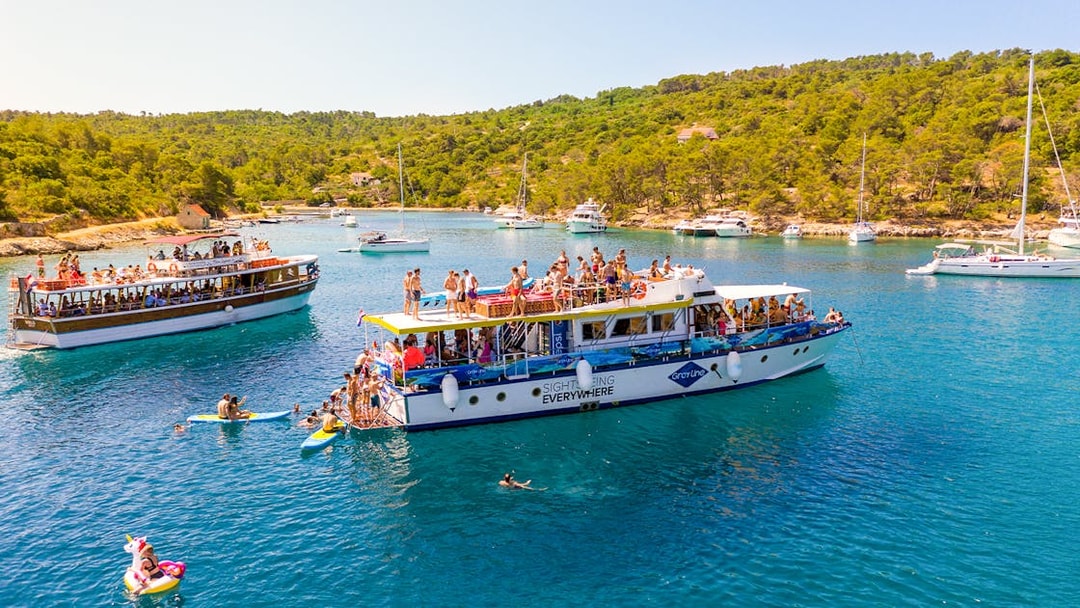 Tourists enjoying a boat cruise in the Blue Lagoon, Šolta, with surrounding yachts and lush greenery.