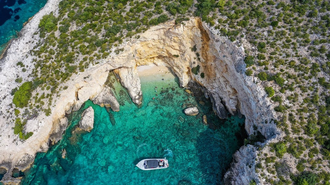 Boat near rocky coastline with clear turquoise water on Split tour to Blue Cave, Vis, and Hvar.