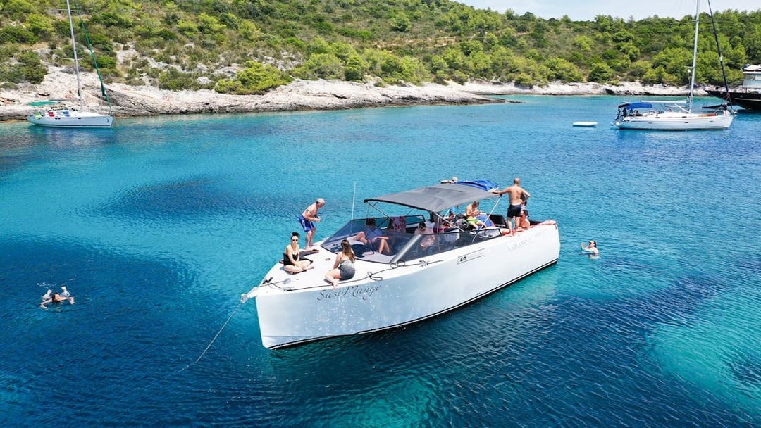 Boat tour with people swimming near Vis, Croatia, surrounded by clear blue water and lush coastline.