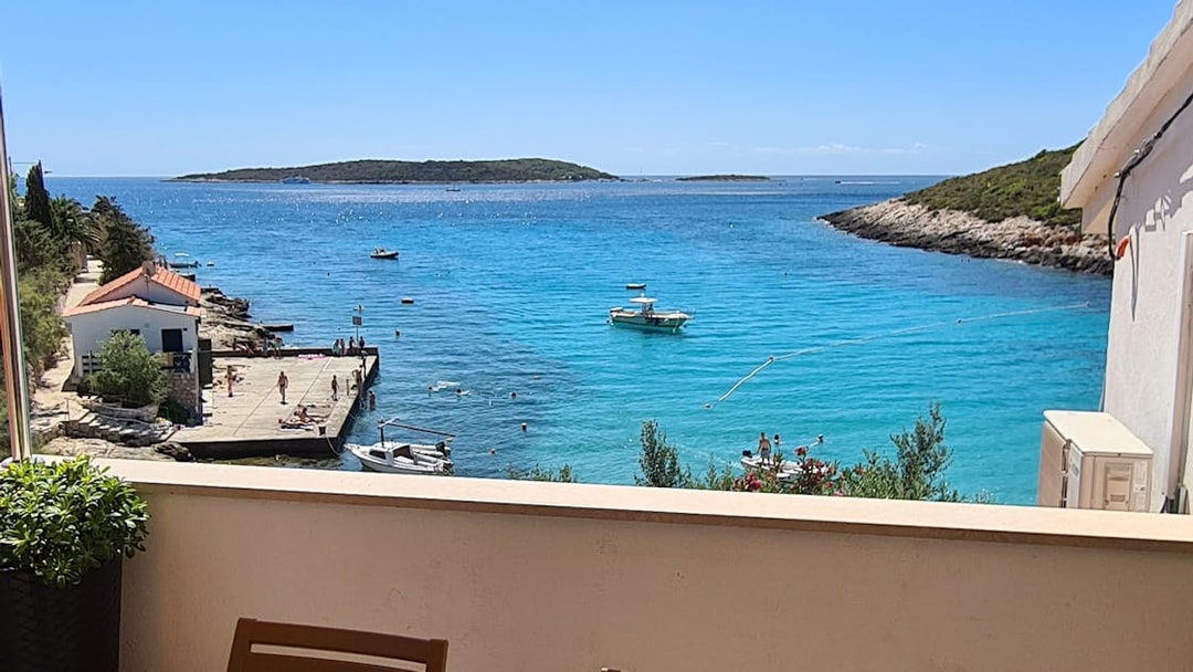 Boats and swimmers in clear blue water near a dock on Vis Island, Croatia.