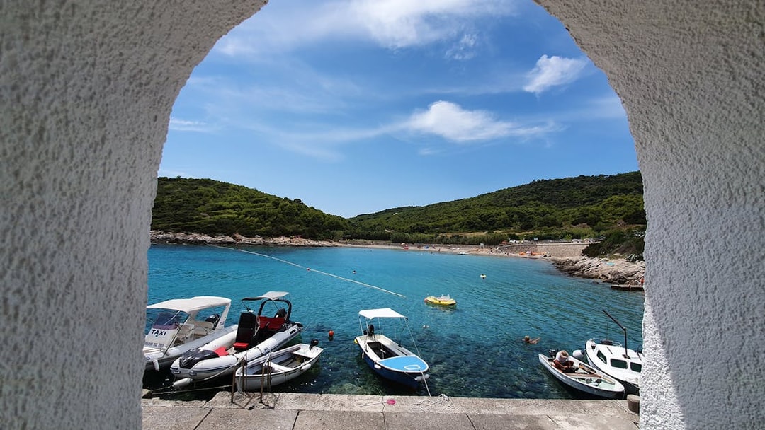 Boats docked in a turquoise bay on Vis Island, Croatia, viewed through an archway.