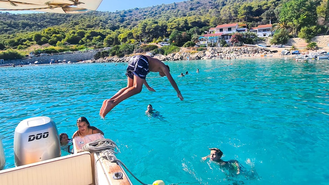 Person diving off a boat into clear blue water near Vis, Croatia, with swimmers nearby.