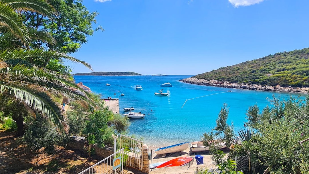 Boats anchored in a turquoise bay near Split, Croatia, with lush greenery and a clear sky.