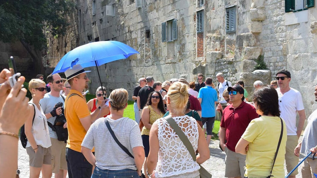 Tour group exploring Diocletian's Palace in Split with a guide holding a blue umbrella.