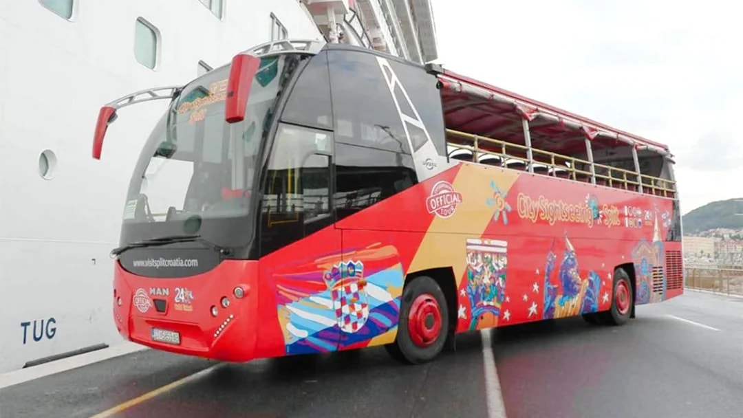 Open-top red tour bus in Split, Croatia, parked near a cruise ship.
