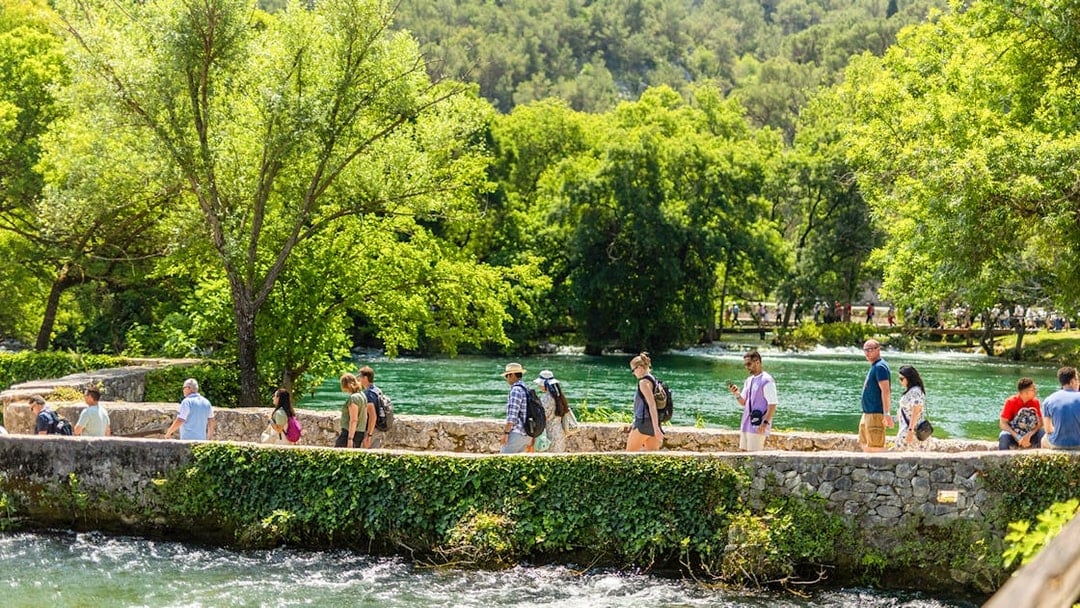 Visitors walking along a stone path by the river at Krka Waterfalls, Split day trip.