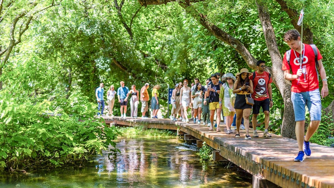 Tourists walking on a wooden path through lush greenery at Krka Waterfalls, Split day trip.