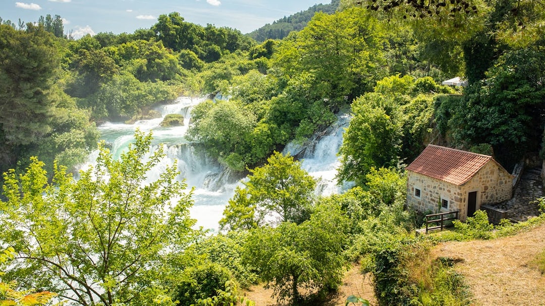 Krka Waterfalls with lush greenery and a stone house, part of a day trip from Split.