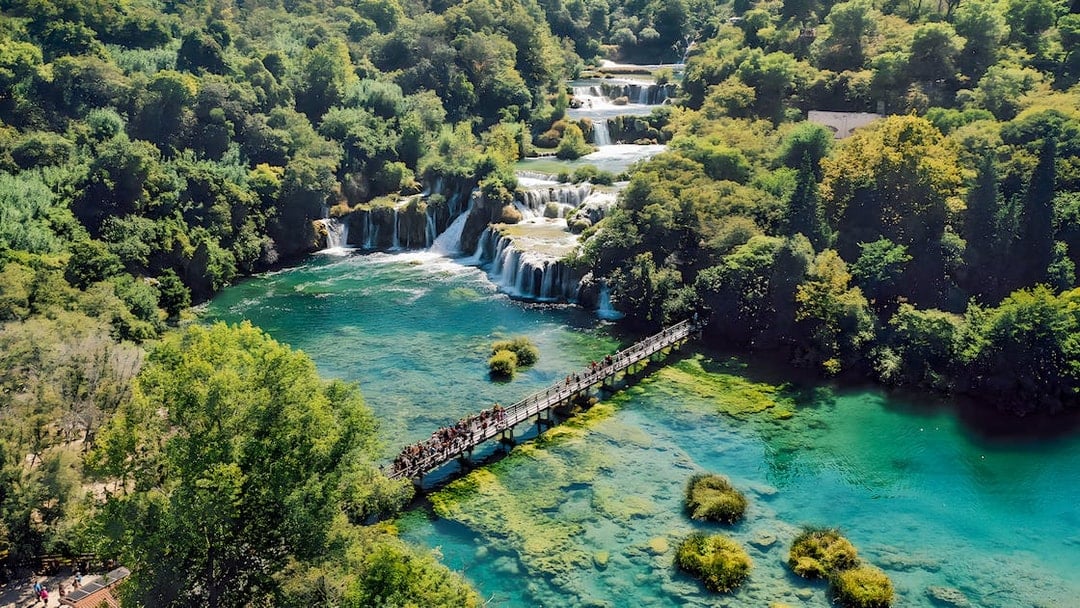 Visitors walking on a bridge over turquoise water at Krka National Park, Croatia.