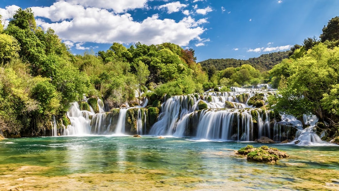 Waterfalls at Krka National Park, Croatia, surrounded by lush greenery under a blue sky.