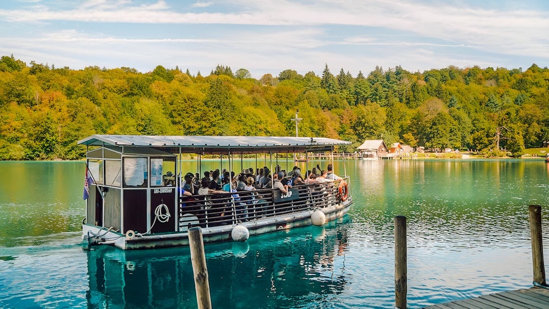 Boat tour on Plitvice Lakes with passengers enjoying scenic views of lush forests.