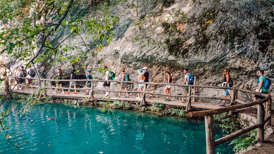 Tour group walking on a wooden path by turquoise water at Plitvice Lakes National Park.
