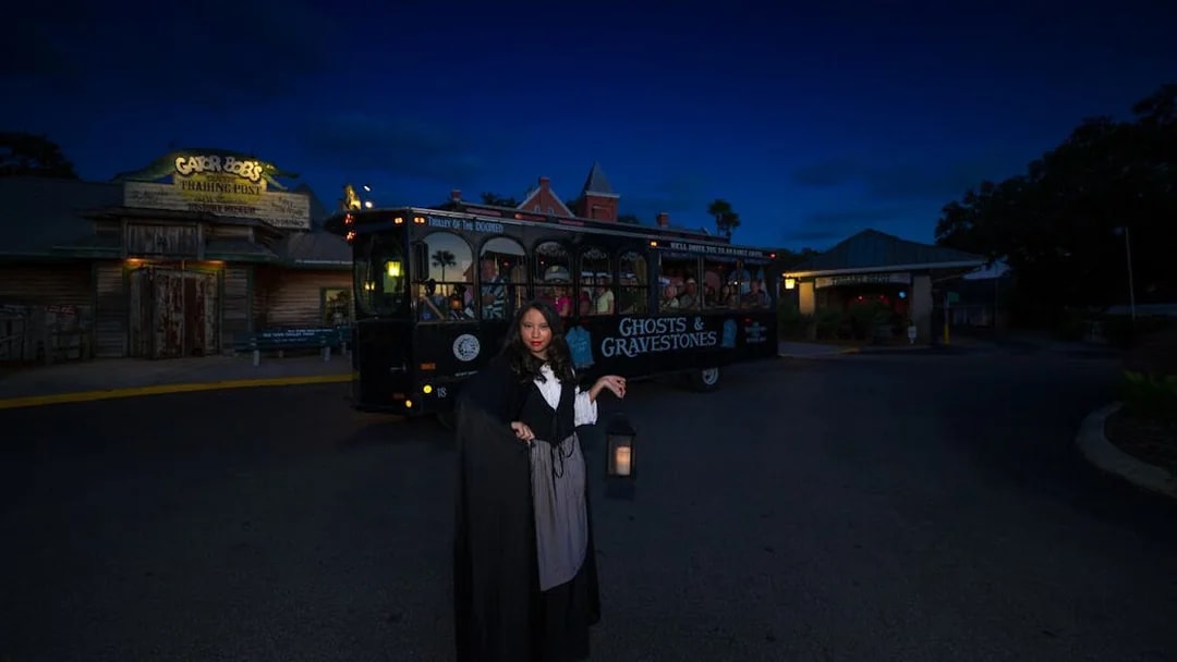 St. Augustine Ghosts & Gravestones tour guide with lantern near trolley at night.