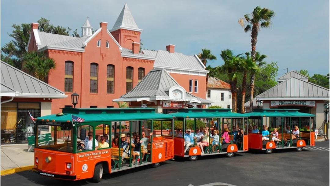 St. Augustine Old Town Trolley with tourists in front of historic red brick building.