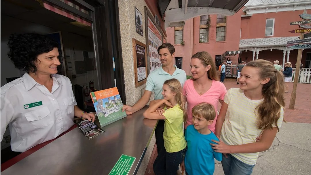 Family receiving St. Augustine Old Town Trolley tickets from a guide at a ticket booth.