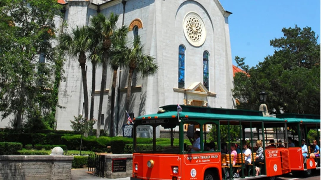 St. Augustine Old Town Trolley in front of historic church with palm trees.