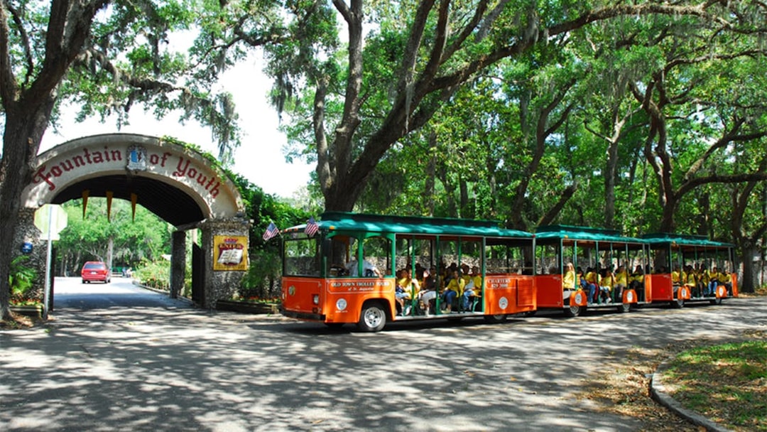 St. Augustine Old Town Trolley at Fountain of Youth entrance, surrounded by trees.