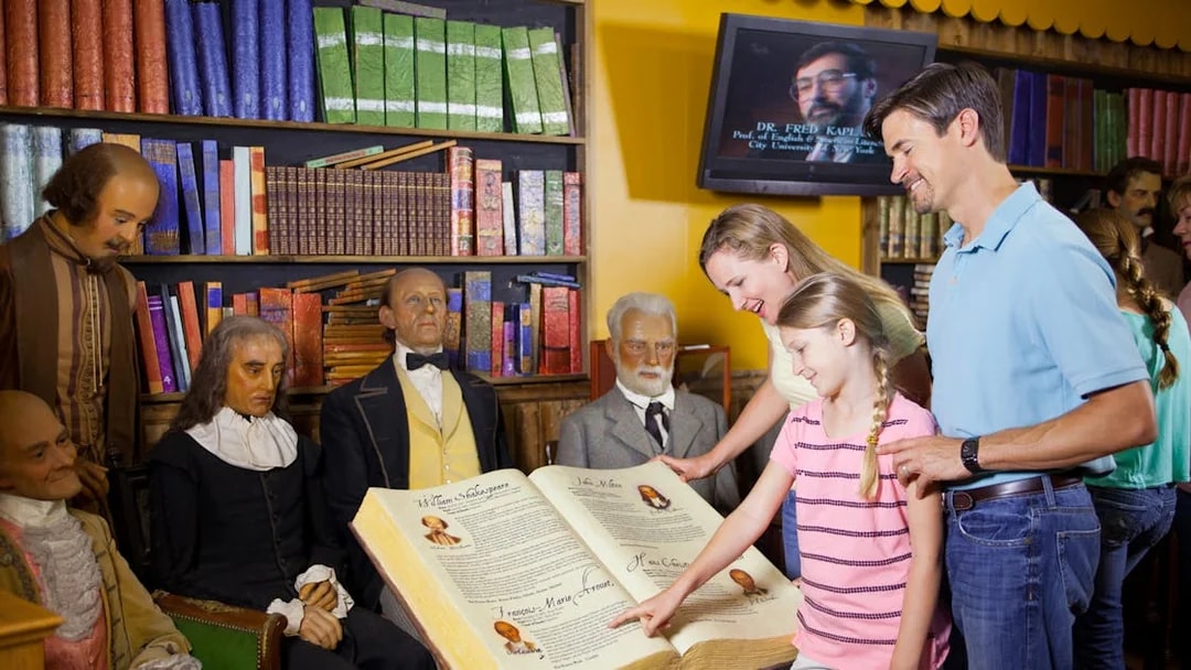 Family exploring wax figures and historical book at St. Augustine Potter's Wax Museum.