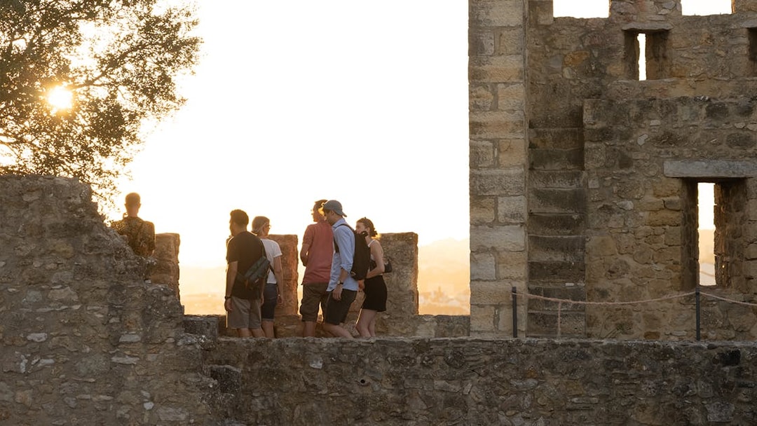 Visitors exploring St. George Castle at sunset, Lisbon, with audio tour on phone.