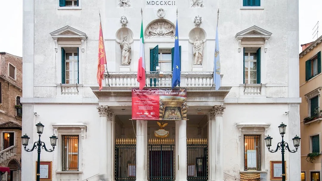 Facade of Teatro La Fenice in Venice, Italy, with flags and statues.