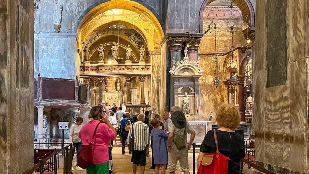 Visitors exploring the interior of St. Mark's Basilica, Venice, with ornate arches and statues.