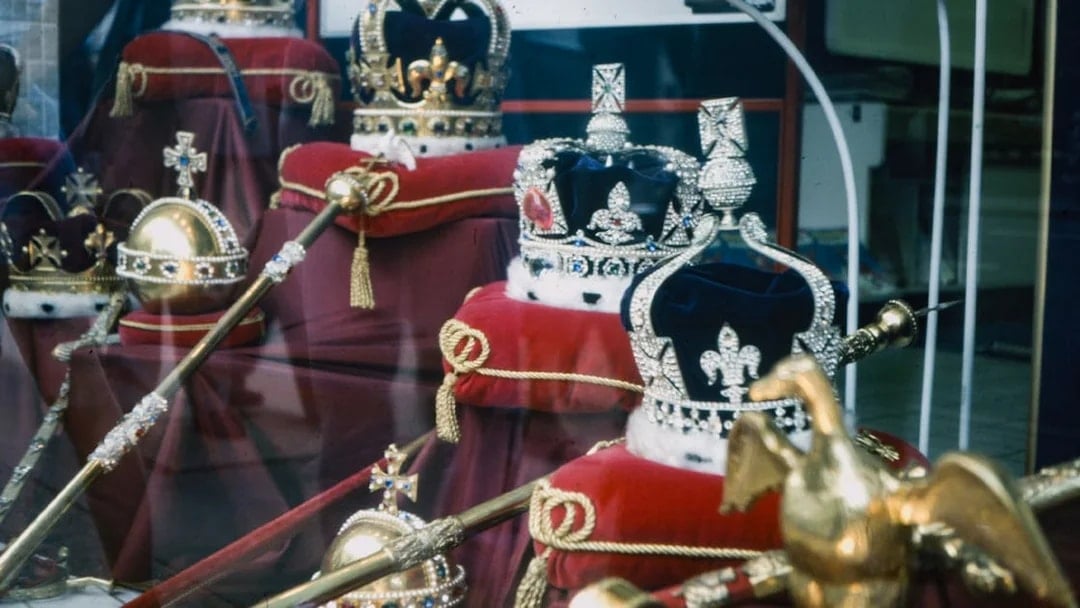 Crown Jewels display in London with crowns and scepters on red cushions.
