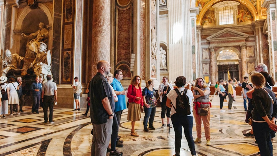Tour group with guide inside St. Peter’s Basilica, Rome, near ornate sculptures.