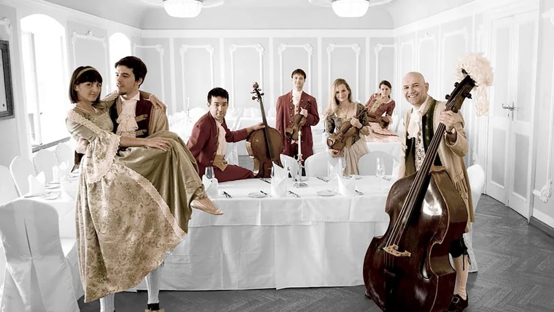 Musicians in period costumes with instruments at a dining table in Salzburg concert setting.