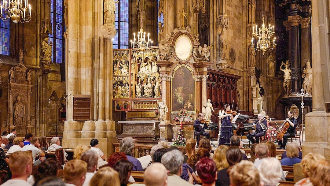 Orchestra performing inside St. Stephen's Cathedral, Vienna, with audience seated in pews.