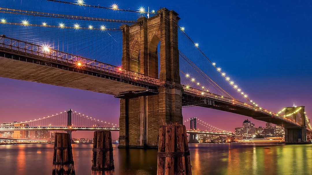 Brooklyn Bridge illuminated at sunset, view from Statue of Liberty & Ellis Island cruise.