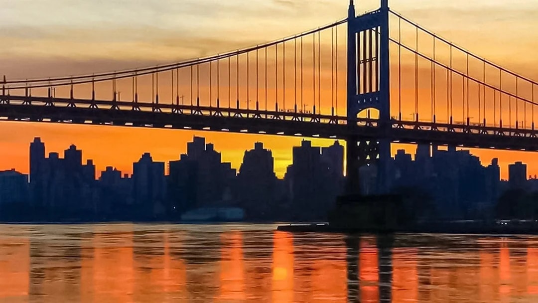Sunset view of New York City skyline and bridge from Statue of Liberty cruise.