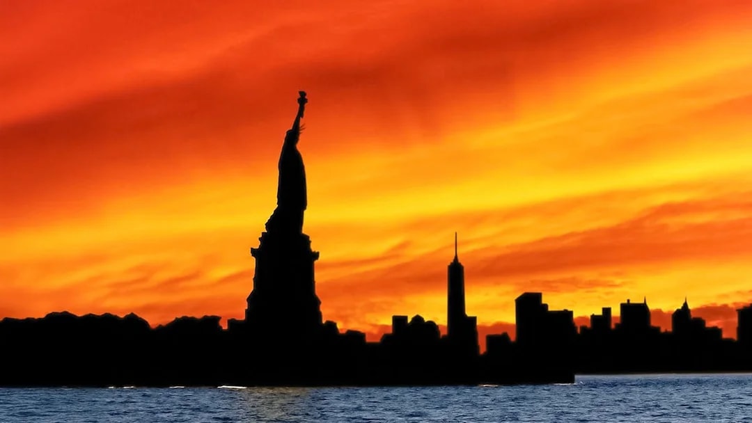Statue of Liberty silhouette against vibrant sunset during Ellis Island cruise.