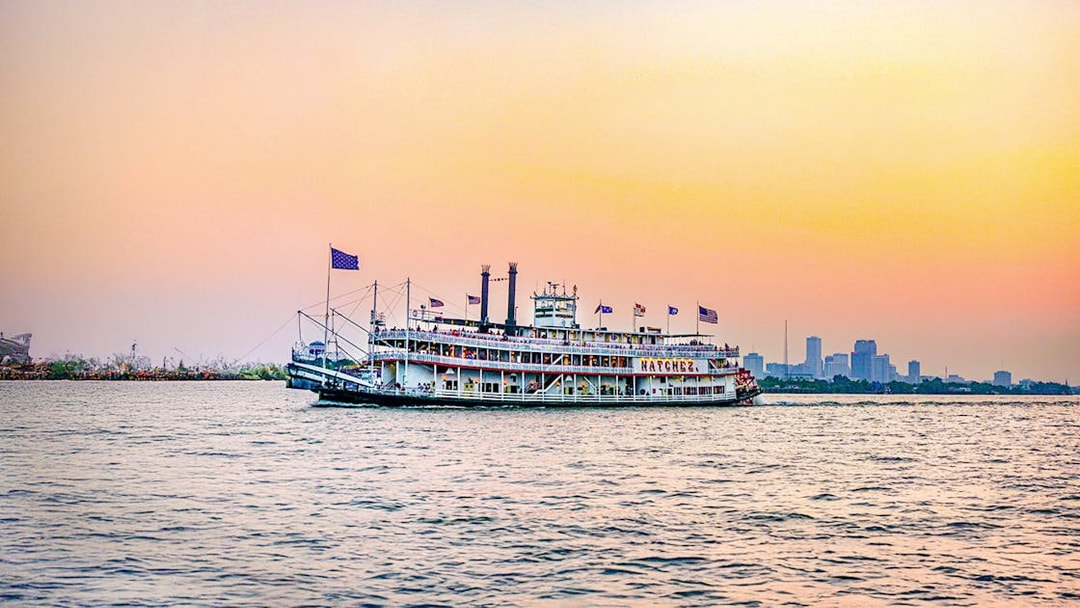 Steamboat Natchez cruising at sunset with city skyline in the background.
