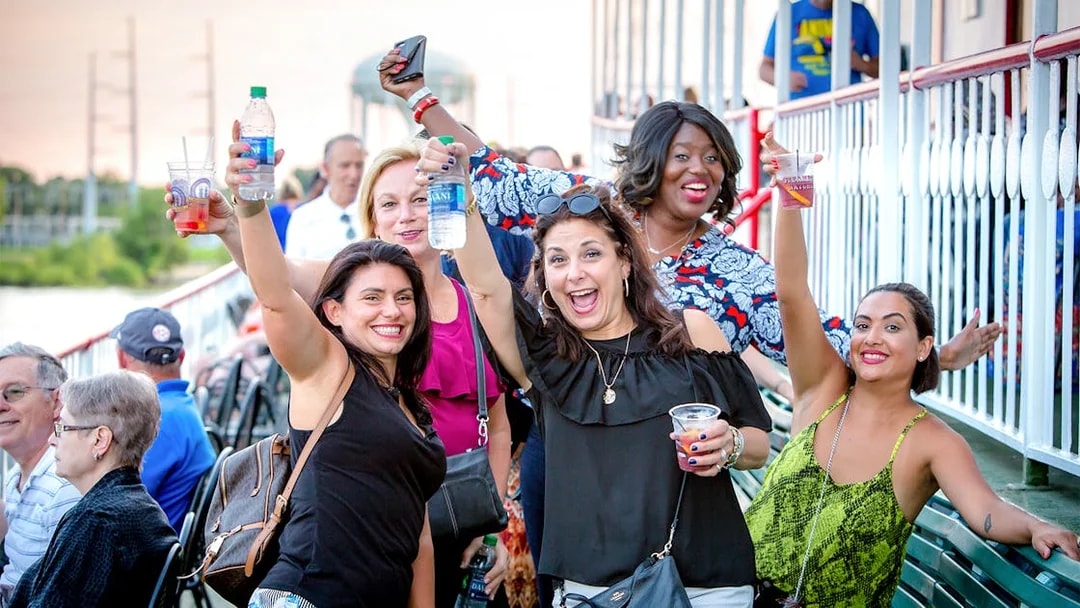 Group of people smiling and raising drinks on the deck of Steamboat Natchez in New Orleans.