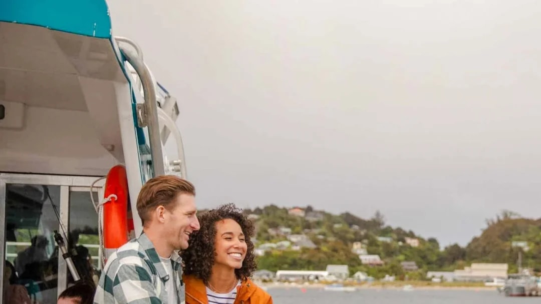 Couple enjoying the view on Stewart Island Ferry, New Zealand coast in background.