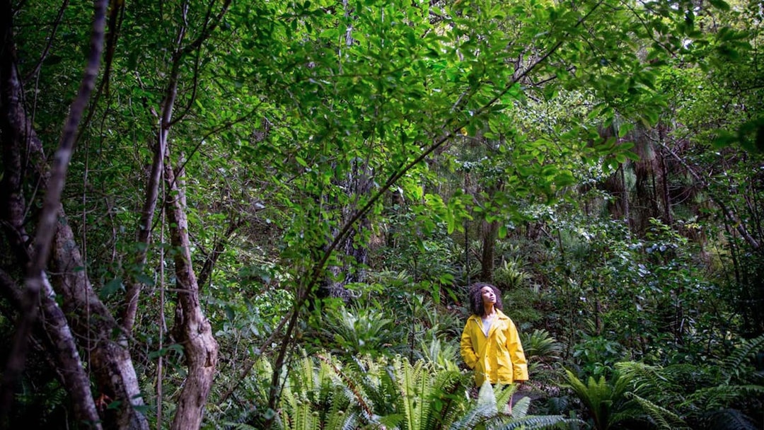 Young woman in a yellow jacket exploring lush island forest.