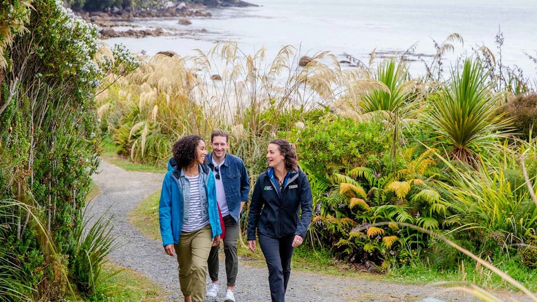 Group walking on a coastal path surrounded by lush greenery on Stewart Island tour.