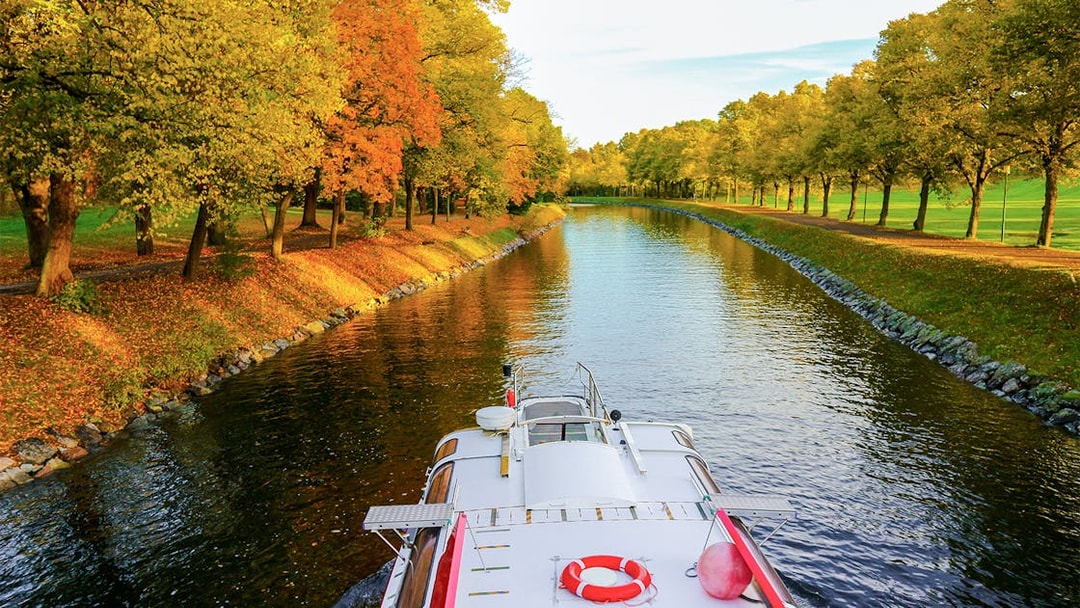 Cruise boat on Djurgrden City Canal surrounded by autumn trees.