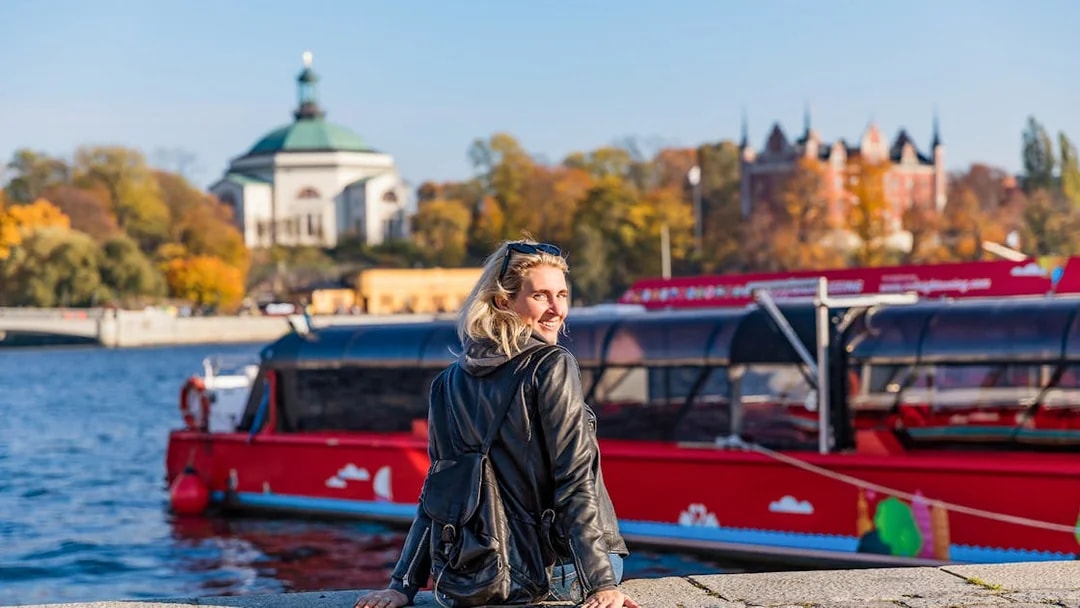 Woman at dock with red boat, ready for Stockholm tour.