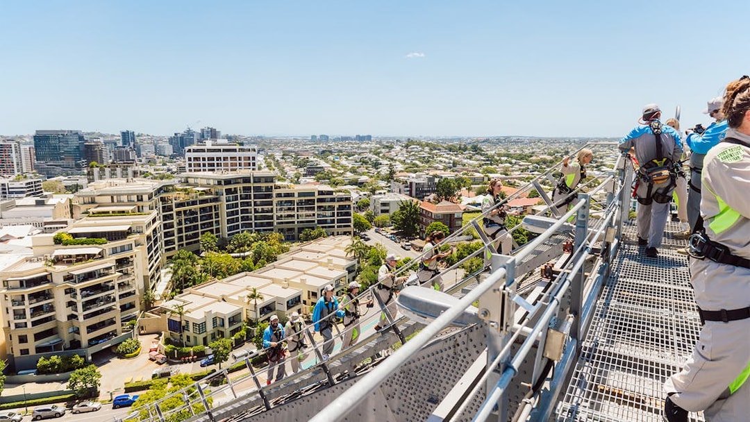 Climbers in harnesses on Story Bridge arch with view of Brisbane cityscape.