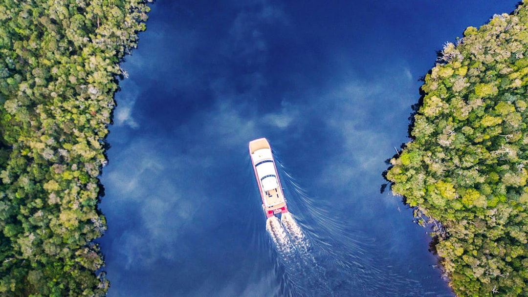 Aerial view of a boat cruising on Gordon River, surrounded by lush greenery, Tasmania.