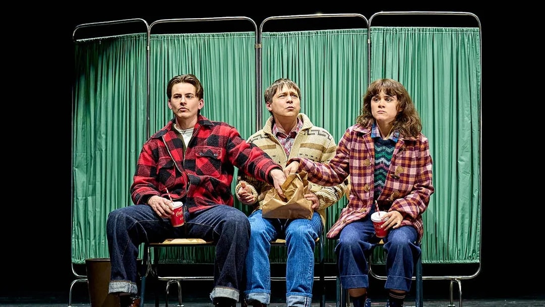 Three people sitting on stage in front of green curtains, part of "Stranger Things: The First Shadow.