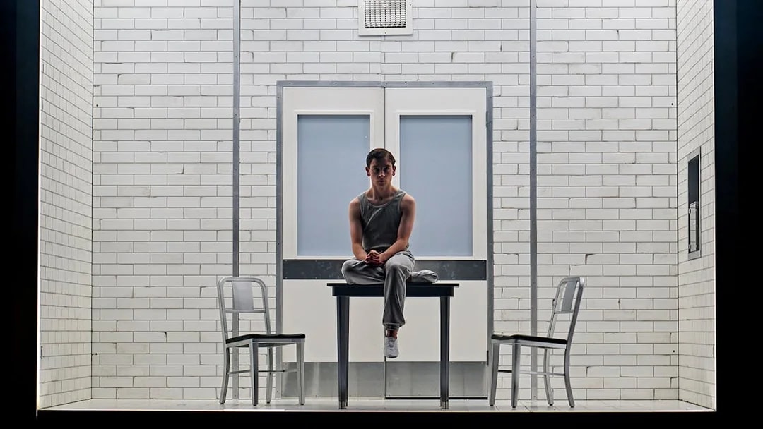 Young person sitting on a table in a tiled room, part of Stranger Things: The First Shadow.