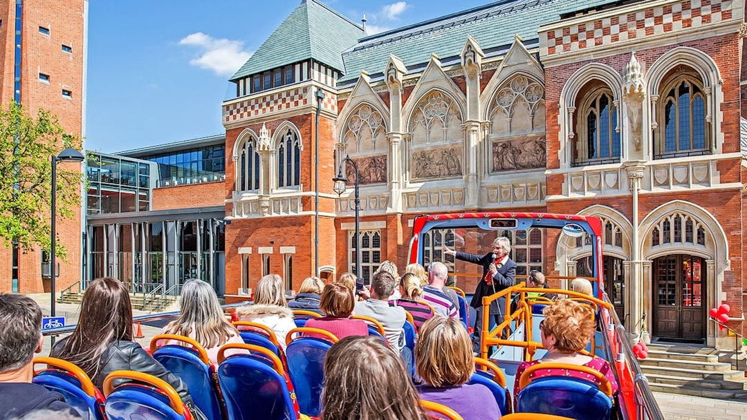 Open-top bus tour in Stratford-upon-Avon passing by historic building with guide speaking to passengers.