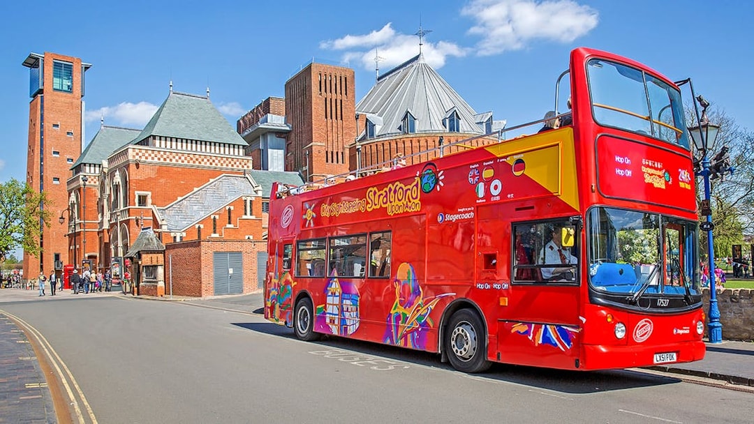 Red double-decker bus on Stratford-upon-Avon street near historic brick building.