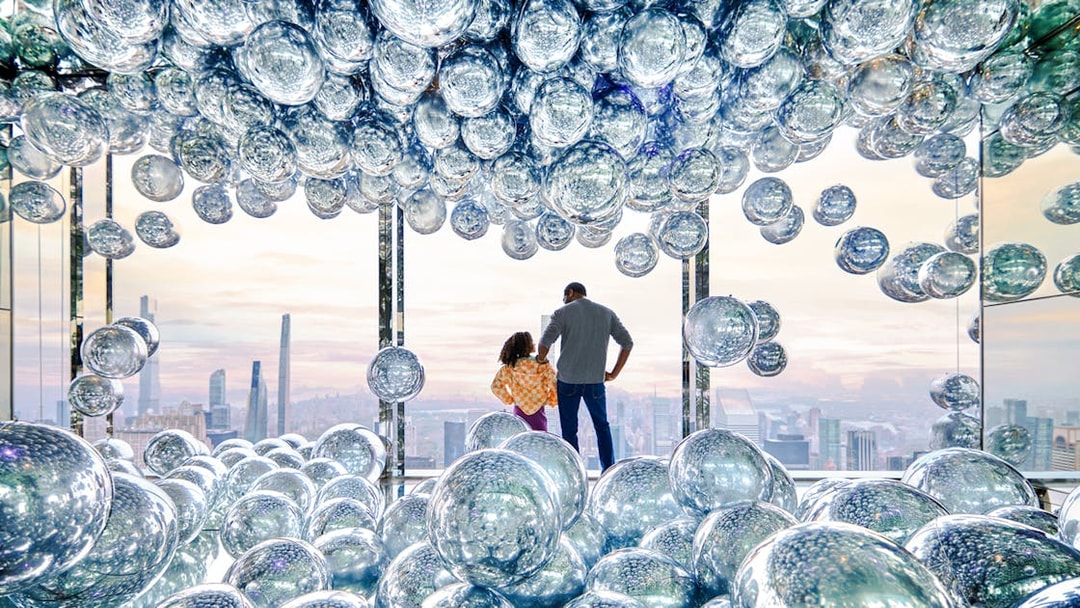 Visitors at SUMMIT One Vanderbilt observation deck with reflective spheres, New York City skyline in view.