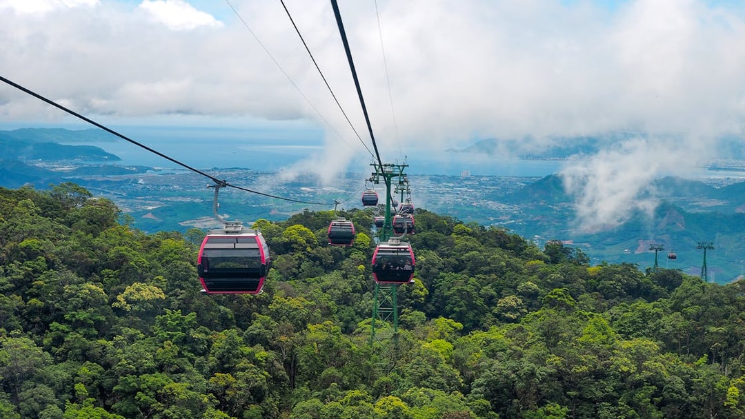 Cable cars over lush forest in Ba Na Hills, Vietnam, with distant city and ocean views.