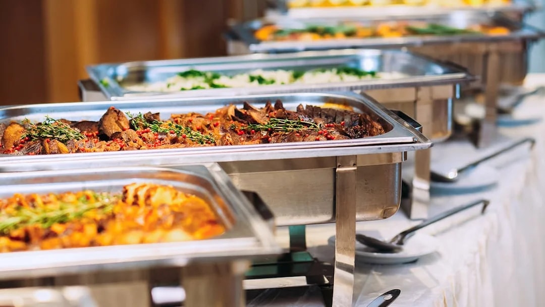 Buffet lunch with assorted dishes in stainless steel trays.