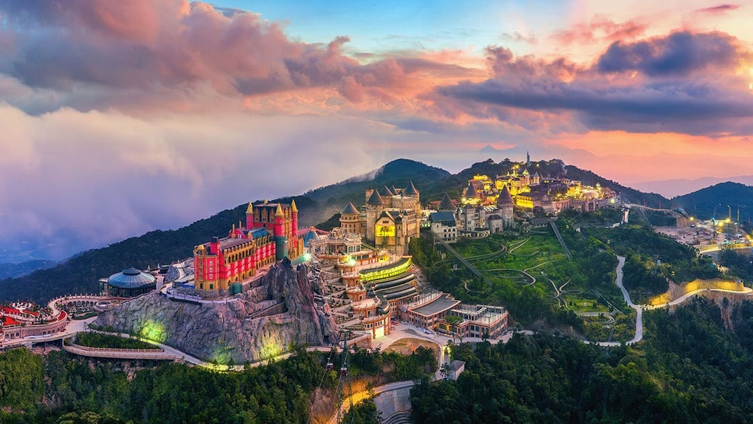 Sunset view of Sun World Ba Na Hills with illuminated castles and lush landscape in Da Nang, Vietnam.